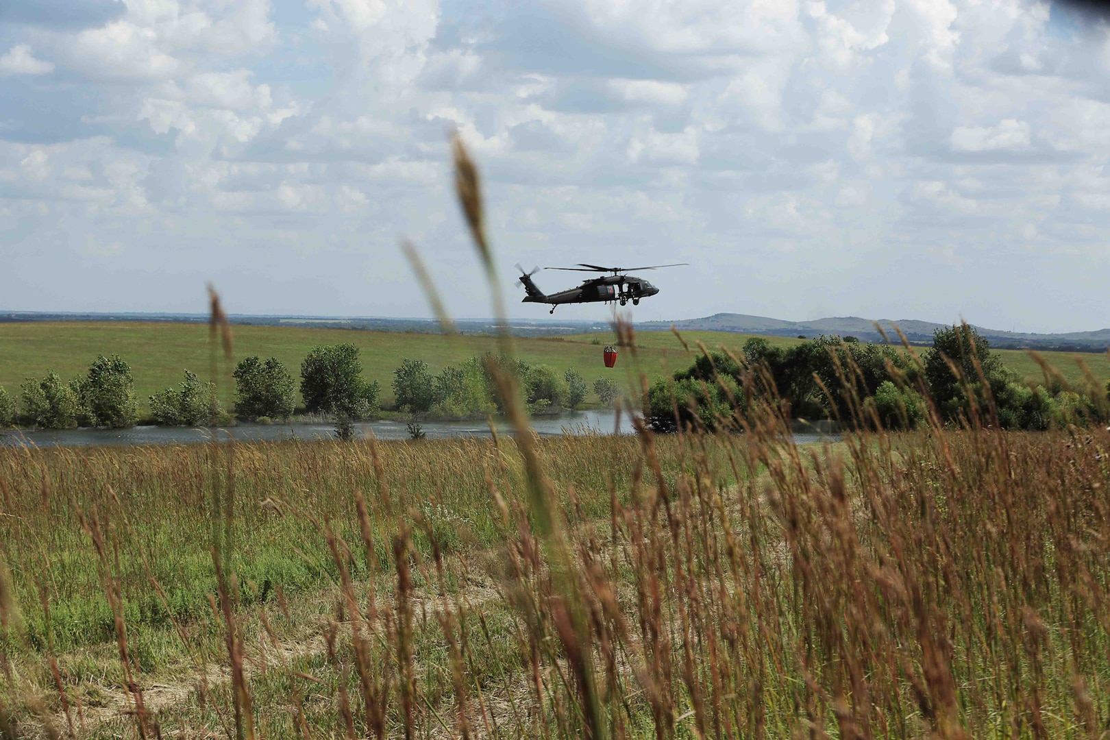 A UH-60 Black Hawk helicopter from the 1st Battalion, 108th Aviation Regiment, fills a bucket with water from a pond during an integrated wildland firefighting exercise with the Kansas Forest Service and the Kansas National Guard at the Smokey Hill Range in Salina, Kansas, Sept. 19, 2019.