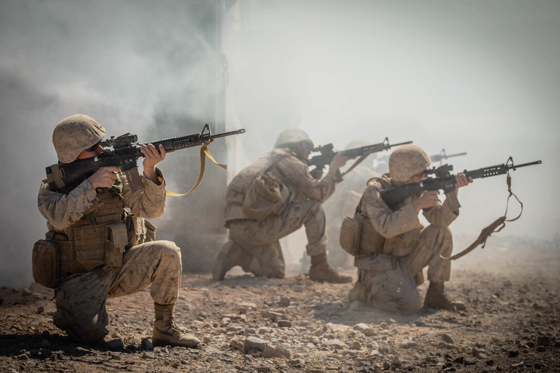 Marines  kneel on the ground pointing their rifles in the air.