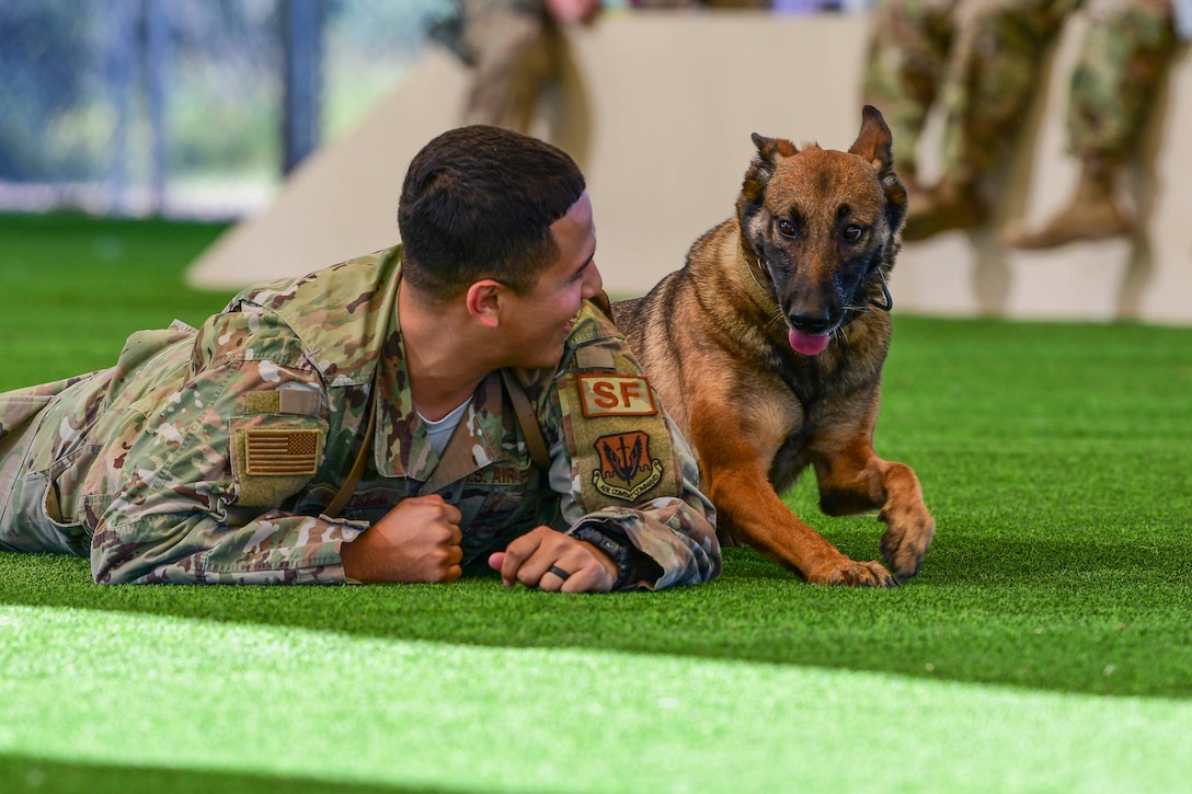 An airman lies on the ground next to a dog.