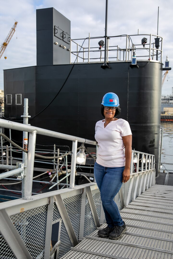 Shop 57 Insulating Mechanic Aisha Clark stands in front of the USS La Jolla (SSN 701), which is currently being converted to a Moored Training Ship (MTS) at NNSY.