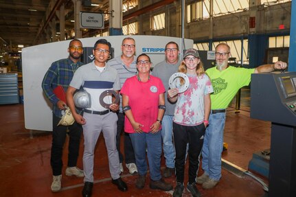 Industrial Tech Barry Forbes, Industrial Engineer Vatanik Chhim, Shop 17 Supervisor Doug Hamilton, Sheet Metal Mechanic Rebekah Regan, Sheet Metal Mechanic Brian Dominici, Sheet Metal Apprentice Danni Edwards, and Sheet Metal Mechanic Ryan Ward celebrate the new hydraulic punching machine joining the ranks in the Sheet Metal Shop (Shop 17).