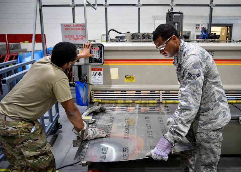 U.S. Air Force Senior Airman Armani Jones and U.S. Air Force Airman 1st Class DeWayne Forward, 305th Maintenance Squadron Fabrication Flight aircraft structural maintenance journeymen, line up a piece of sheet metal to be cut on Joint Base McGuire-Dix-Lakehurst, New Jersey, Oct. 16, 2019. Aircraft structural maintenance Airmen restore and upkeep aircrafts on Joint Base MDL by creating new parts out of sheet metal. The mission of the 305th MXS is to enhance global response by providing world class systems, support equipment, munitions and aircraft maintenance. (U.S. Air Force photo by Senior Airman Jake Carter)
