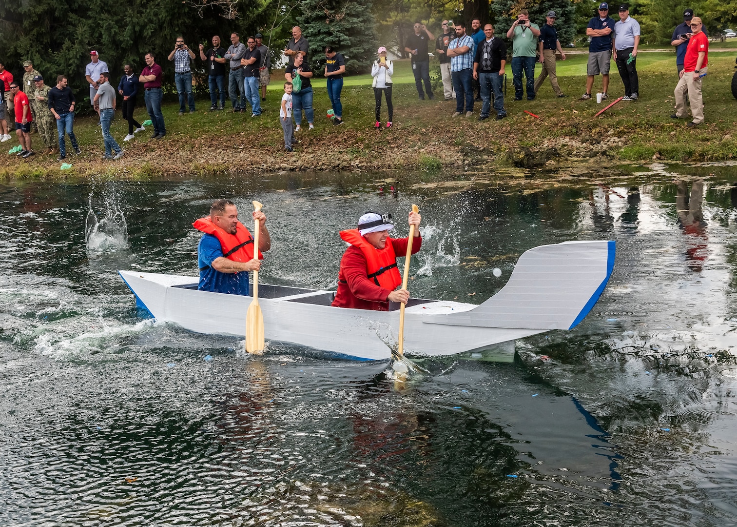 Two men paddle a canoe made of cardboard