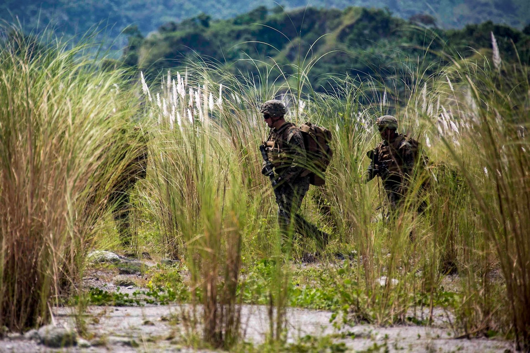 Marines walk through tall grass.