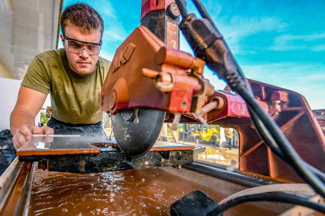 An airman uses a machine to cut tile.