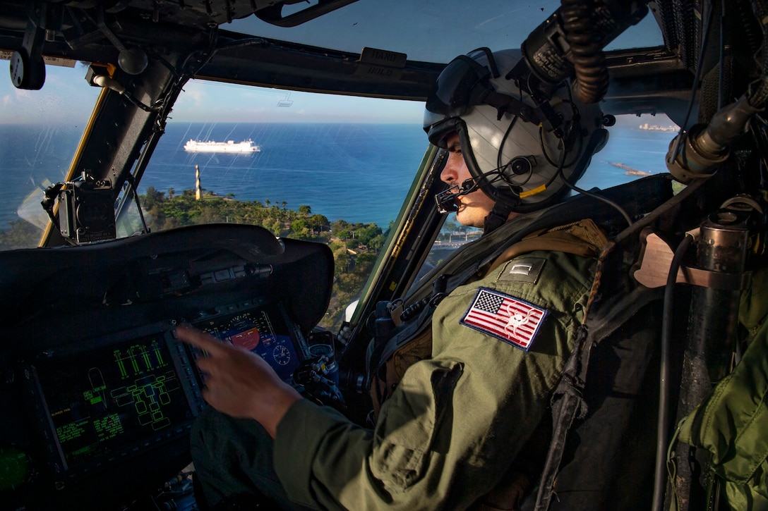 A pilot flies an aircraft while a ship is seen on the ocean below.