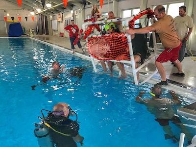 Soldiers with the 28th Expeditionary Combat Aviation Brigade prepare to be submerged in a Shallow Water Egress Trainer chair, pushed by civilian and military instructors. The Soldiers had to demonstrate water survival skills, simulating exiting a submerged helicopter, during training at the pool at Somerset Area High School Oct. 19, 2019.