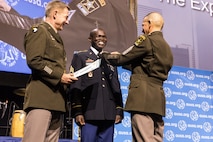 Sgt. 1st Class Anthony Lodiong receives his Expert Soldier Badge from Army Chief of Staff Gen. James C. McConville and Sgt. Maj. of the Army Michael A. Grinston at the at the Eisenhower Luncheon during the Association of the United States Army annual meeting and exposition at the Walter E. Washington Convention Center in Washington, D.C. Oct. 14. (Photo courtesy of the U.S. Army)
