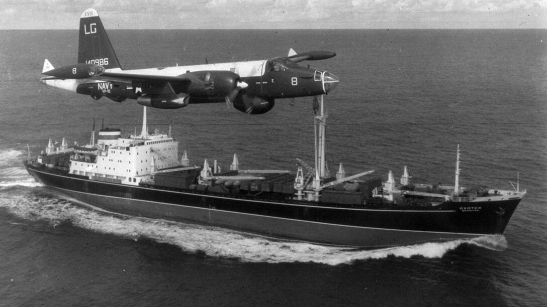 A U.S. Navy P2V Neptune flies over a Soviet freighter in a black and white photo from 1962