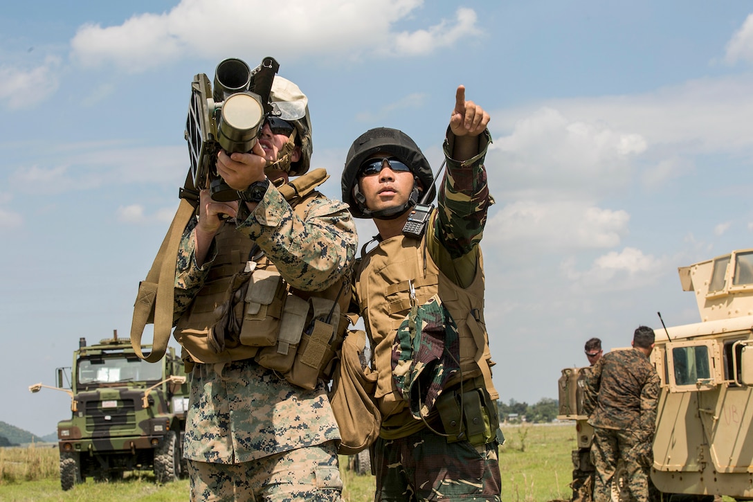 A Marine aims a weapon as a Philippine service member points into the distance.