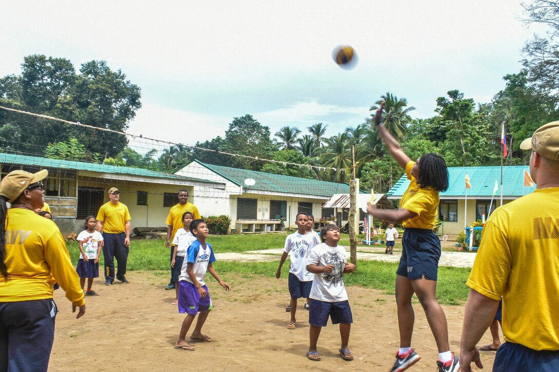 A group of sailors play volleyball with young students.
