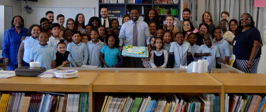 Ryan McLeod, DLA Troop Support Project G.I.V.E. coordinator, center, holds a cake and poses with students and tutors during the Project G.I.V.E. pizza party at the Benjamin Franklin Elementary School Oct. 1, 2019 in Philadelphia.
