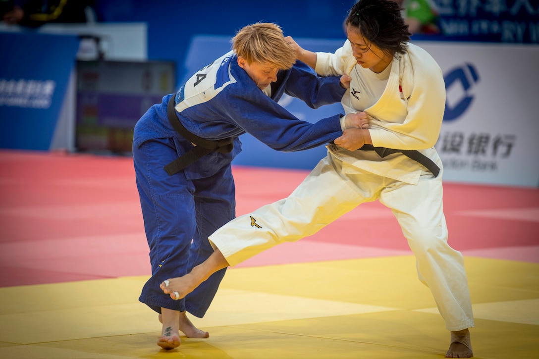 One woman holds onto a second woman who is trying to trip her during a judo match.