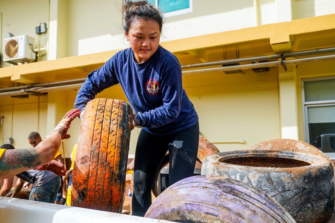 A sailor lifts a painted tire near a stack of tires outside a school.