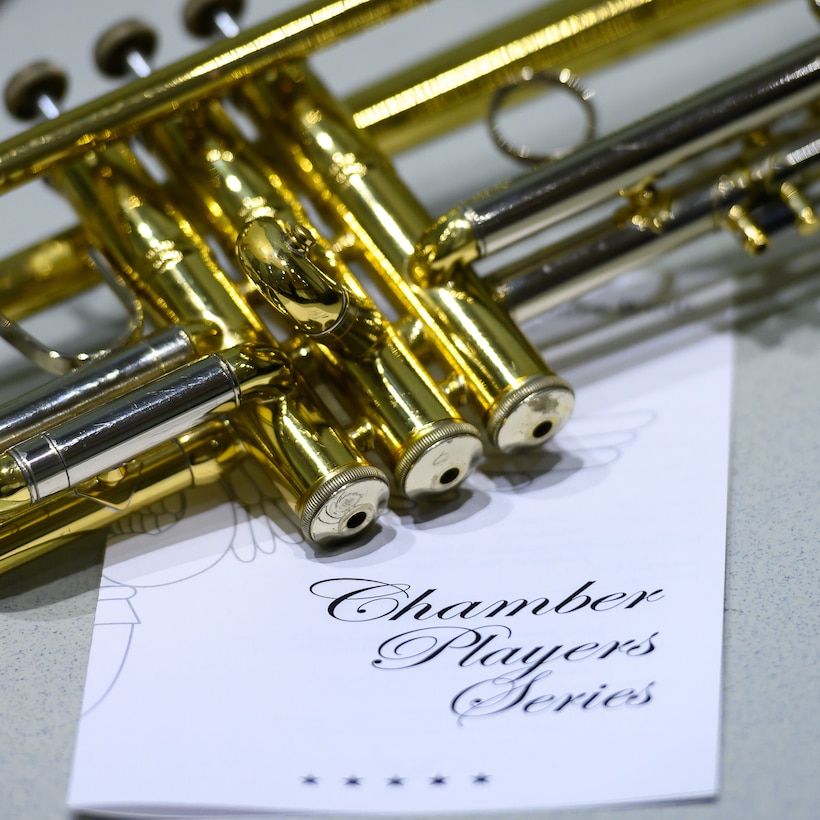 A trumpet is pictured laying on its side on top of a concert program with the words "Chamber Player Series" printed in large letters on the front cover.