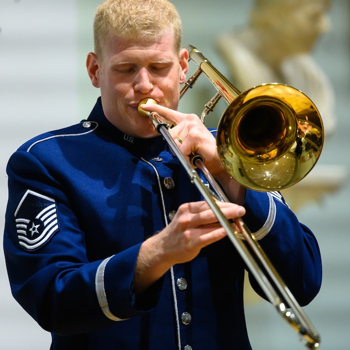 An Air Force trombonist performs a solo. He is wearing a dark blue Air Force uniform.