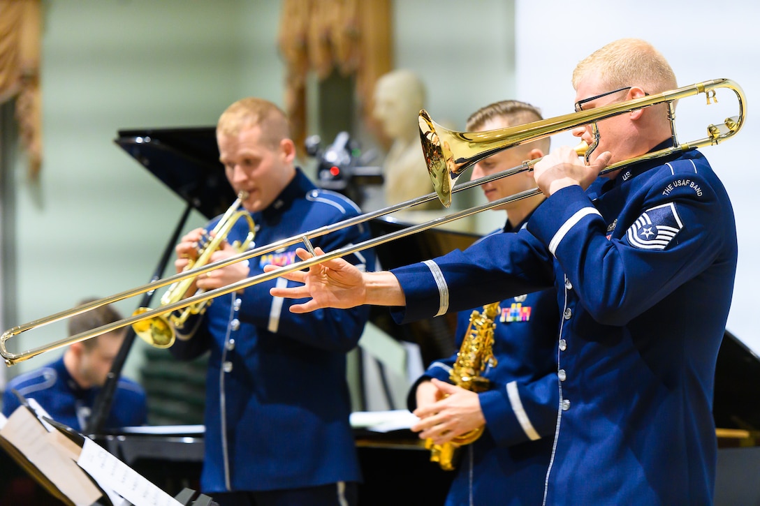 Four Air Force musicians--a trombonist, trumpeter, saxophonist, and pianist--are performing. Each are wearing dark blue Air Force uniforms.