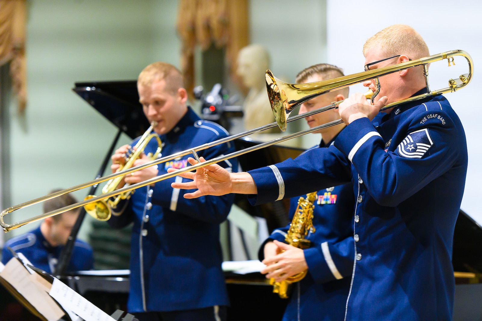 Four Air Force musicians--a trombonist, trumpeter, saxophonist, and pianist--are performing. Each are wearing dark blue Air Force uniforms.