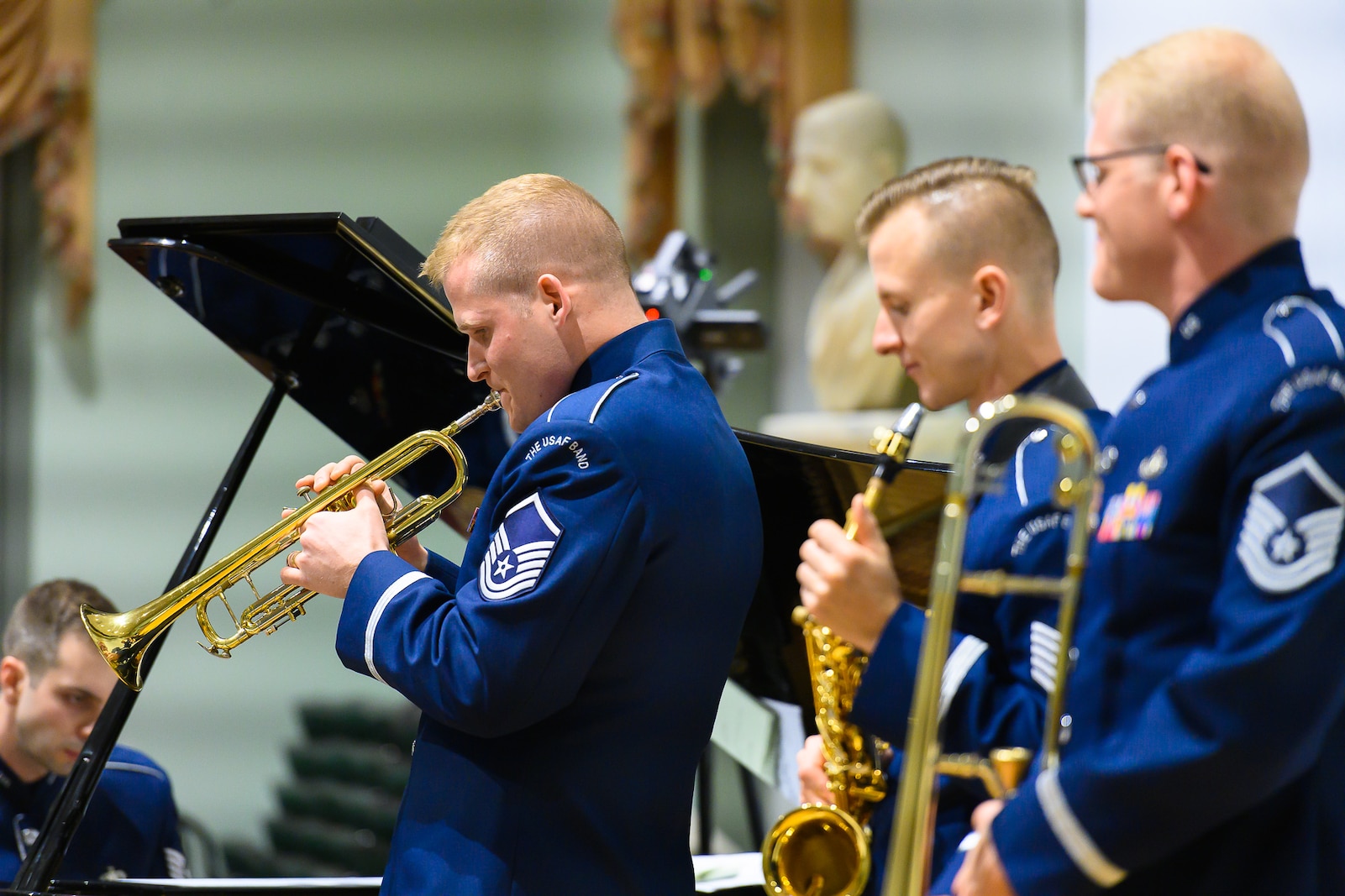 Four Air Force musicians--a trombonist, trumpeter, saxophonist, and pianist--are performing. Each are wearing dark blue Air Force uniforms.