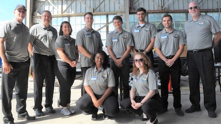 IMAGE: DAHLGREN, Va. – (Sept. 19, 2019) - The Naval Surface Warfare Center Dahlgren Division (NSWCDD) Sly Fox Mission 26 team and mentors are pictured moments before demonstrating PERSEUS to more than two dozen observers at a demonstration held for distinguished visitors. The junior scientists and engineers briefed military, government civilians, and defense contractors five times over the course of two days on their development of PERSEUS – the most recent effort in a line of projects solving the integration of high-powered electric weapon systems and electric propulsion systems. Sly Fox team members left to right, back row: Tony Scaramozzi (mentor), Chester Petry (mentor), Emily Rabin, Tyler Boitnott, Michael Joram, Kyle Dalton, Steven Lohrey, and Bill Walsh (mentor). In front, left to right: Dominique James and Bridgett Burg.  (U.S. Navy photo/Released)