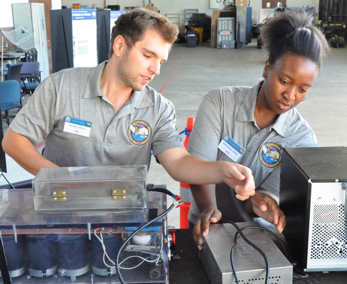 IMAGE: DAHLGREN, Va. (Sept. 19, 2019) – Steven Lohrey, left, and Dominique James prepare to demonstrate PERSEUS – the most recent effort in a line of projects solving the integration of high-powered electric weapon systems and electric propulsion systems aboard U.S. Navy ships. They were among a seven-member team of Sly Fox Mission 26 junior scientists and engineers who briefed military, government civilians, and defense contractors five times over the course of two days on their development of PERSEUS.  (U.S. Navy photo/Released)