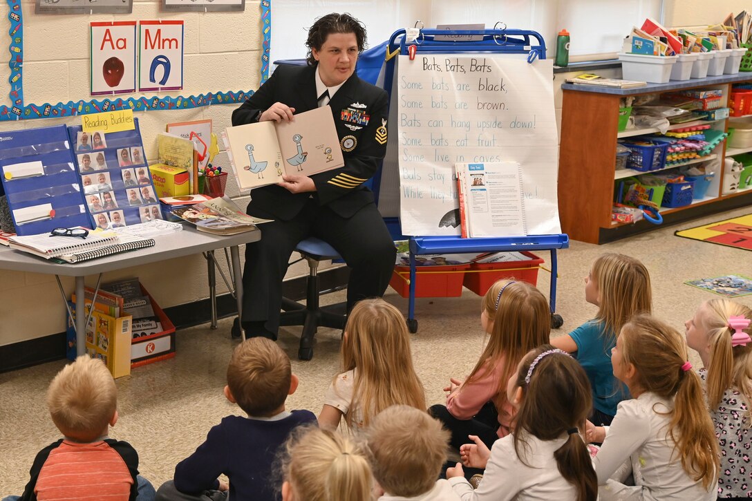 A sailor reads to a group of children.