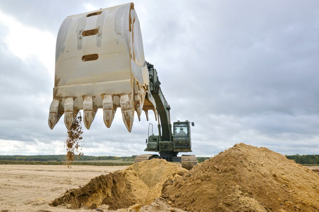 The bucket of an excavator drops dirt on a mound.