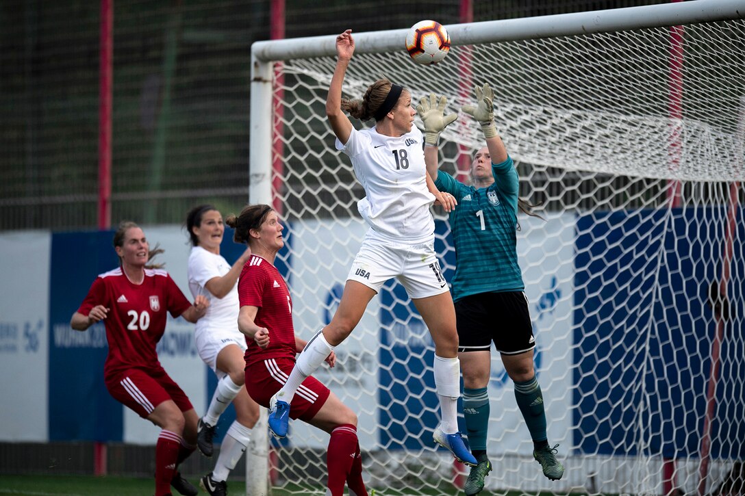 An Air Force athlete leaps in the air as a soccer ball flies toward the top of a goal and a German goalie tries to catch it.
