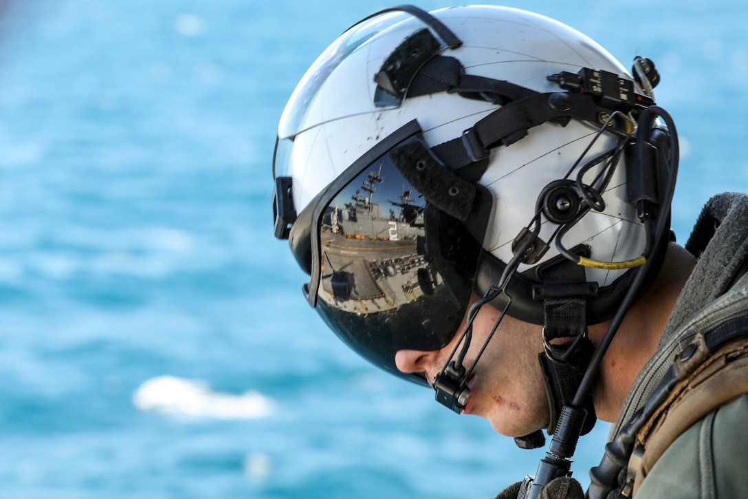 The eyepiece of a sailor's helmet reflects the view of a ship, as aqua water frames the view.