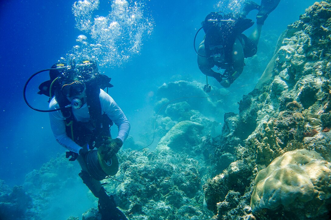 Two divers maneuver in rich blue water.