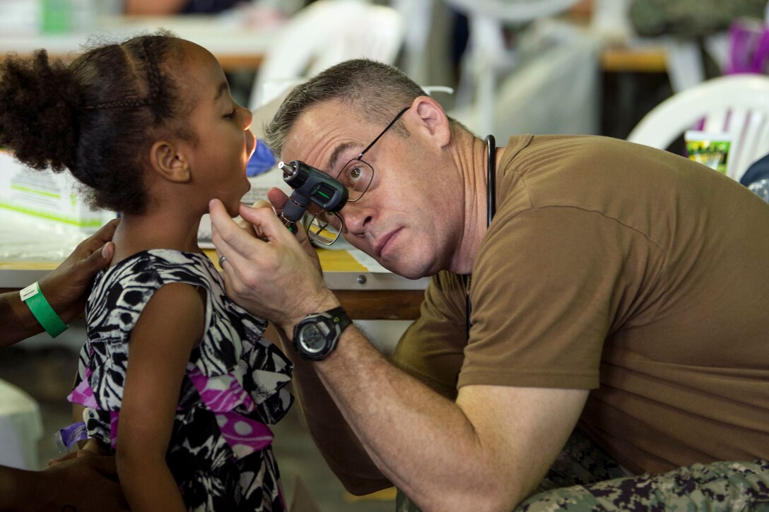 A Navy doctor uses a light to look into a girl's mouth.