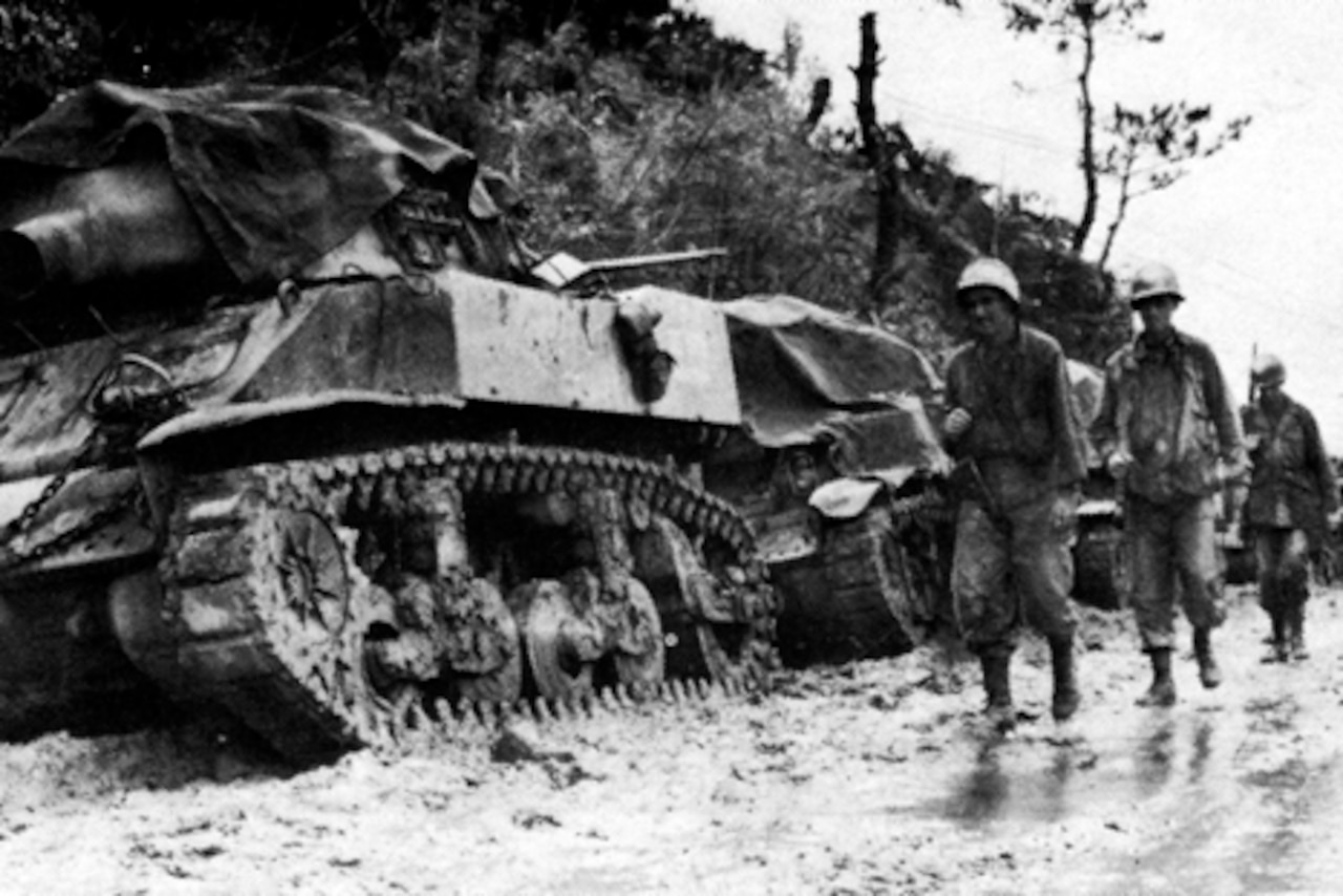 Soldiers trudge past tanks in the mud.