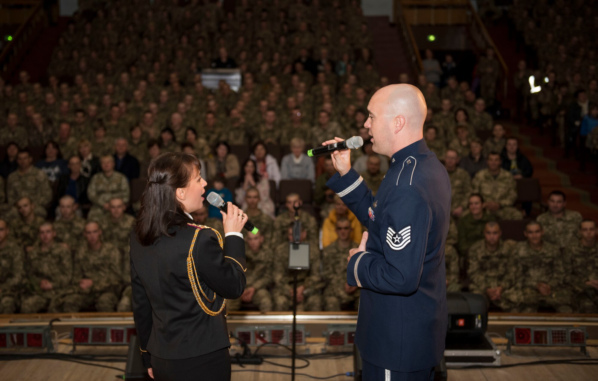 U.S. Air Force Tech. Sgt. Ben Huseby, U.S. Air Forces in Europe Ambassadors Jazz Band vocalist, and Irina Kulik, Ukrainian National Presidential Orchestra vocalist, perform a duet during a concert with the USAFE Band and Ukrainian National Presidential Orchestra at the 169th Training Center in Desna, Ukraine, Oct. 16, 2019. The USAFE Band traveled to six cities in central and western Ukraine October 6-20, 2019 to conduct the “Music of Freedom” tour, which celebrated the shared spirit of freedom and enduring partnership between U.S. and Ukrainian armed forces. (U.S. Air Force photo by Airman 1st Class Jennifer Zima)