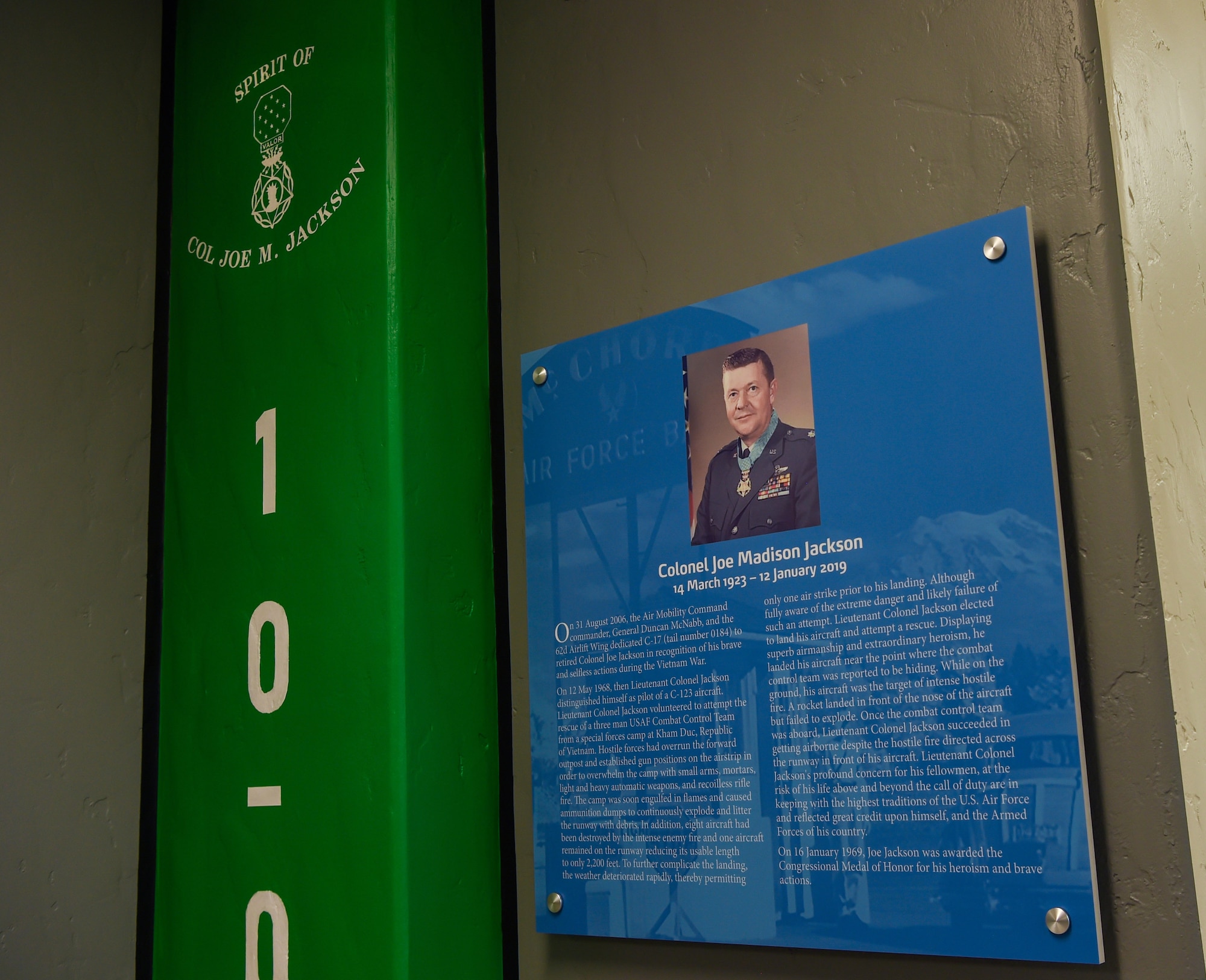 A commemorative plaque hangs on the wall in the newly updated Heritage Hall in the wing headquarters building honoring retired Col. Joe Jackson, Air Force Medal of Honor recipient, at Joint Base Lewis-McChord, Wash., Oct. 21, 2019. In 2006, a McChord C-17 Globemaster III was dedicated to Jackson in recognition of his actions during the Vietnam War. (U.S. Air Force photo by Senior Airman Tryphena Mayhugh)