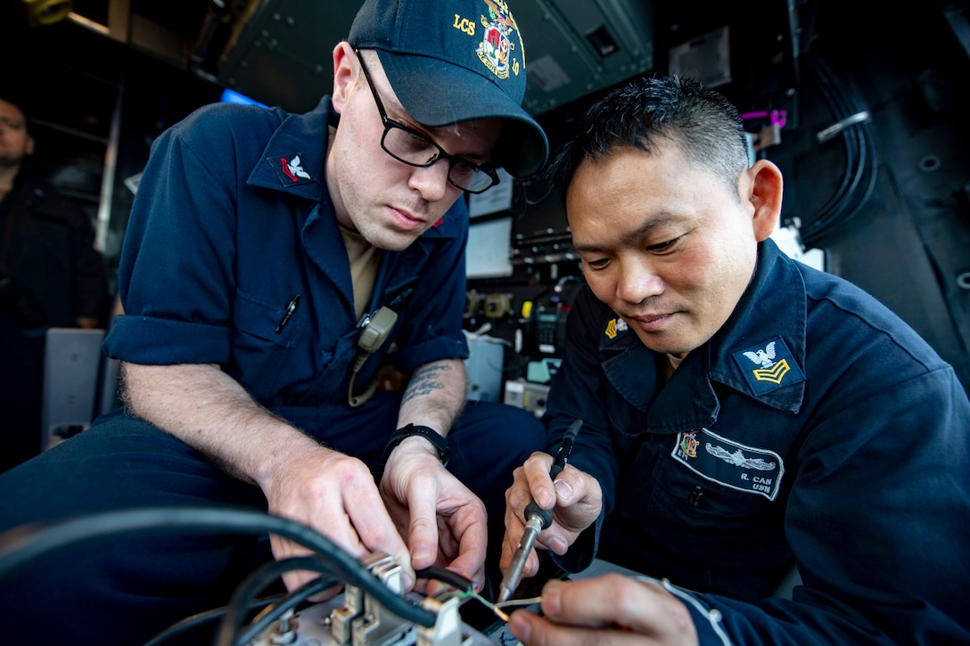 Two sailors solder wires on a device.
