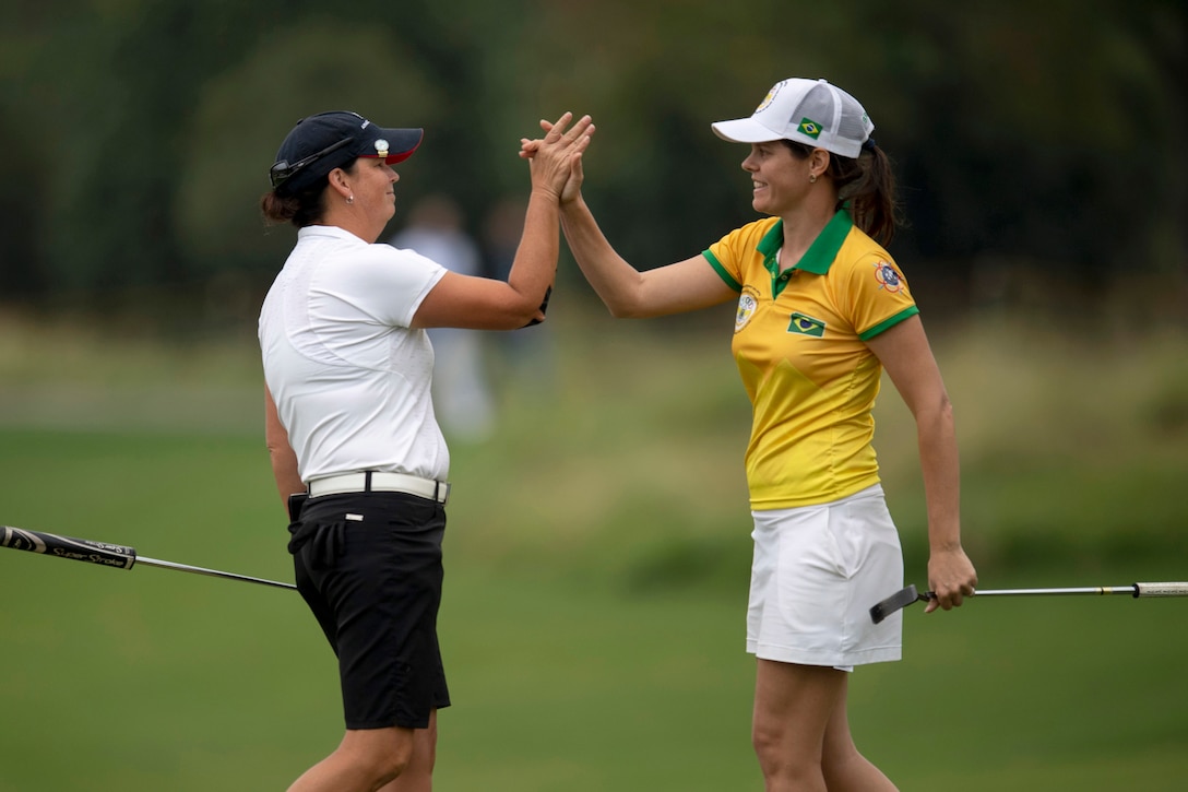 An Air Force golfer high-fives a Brazilian golfer on a course.