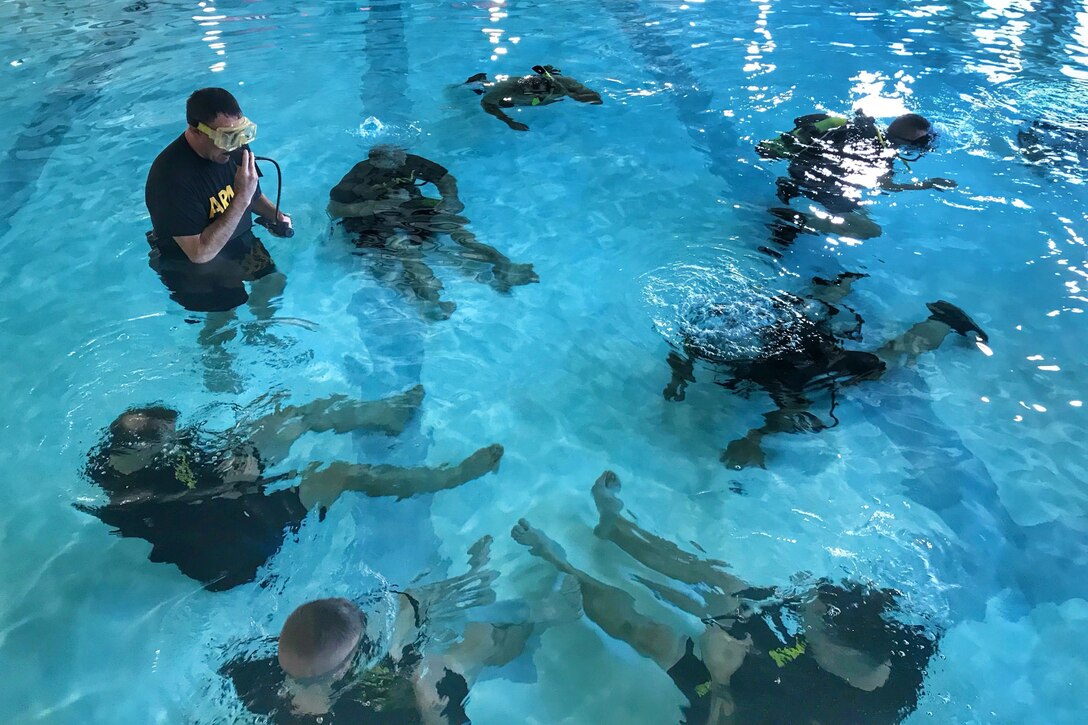 A group of soldiers sit in a pool underwater in  circle; one soldiers stands above water.