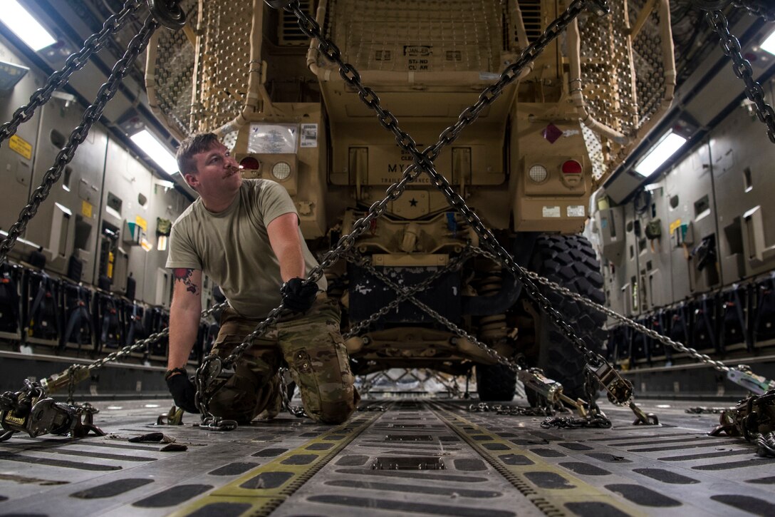 An airman pulls on a chain that is surrounding a military vehicle.