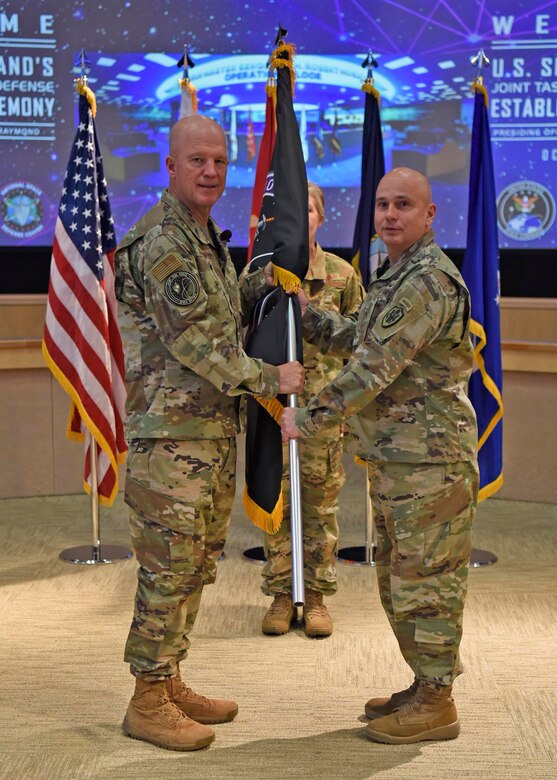 Air Force Gen. John "Jay" Raymond (left), U.S. Space Command commander, presents colors to U.S. Army Brig. Gen. Thomas James, Joint Task Force Space Defense commander, to recognize the establishment of the new task force during a ceremony on Schriever Air Force Base, Colorado, Oct. 21, 2019. James, an Army space operations officer, has served in space-related assignments for the past 19 years. (DOD photo by Patrick Morrow)
