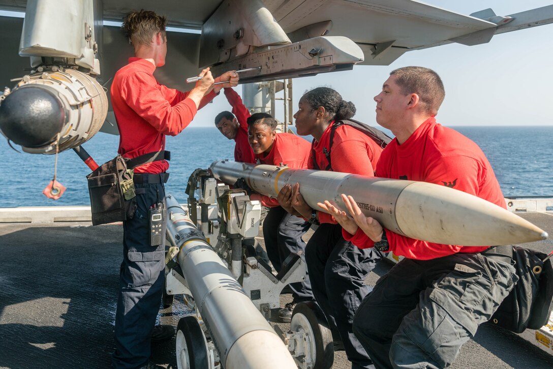 Sailors lift ordnance into a military jet.