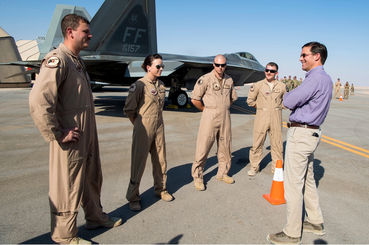 Defense Secretary Dr. Mark T. Esper talks to four airmen standing on a flightline by a plane.