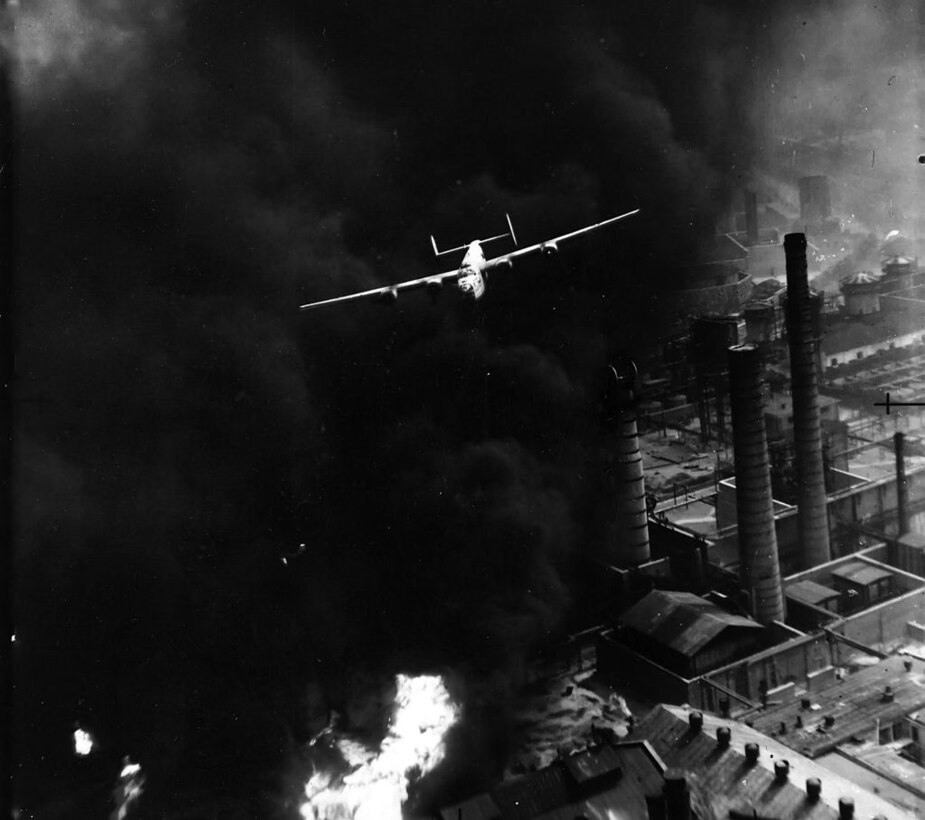 Aircraft flies over a smoking oil refinery.