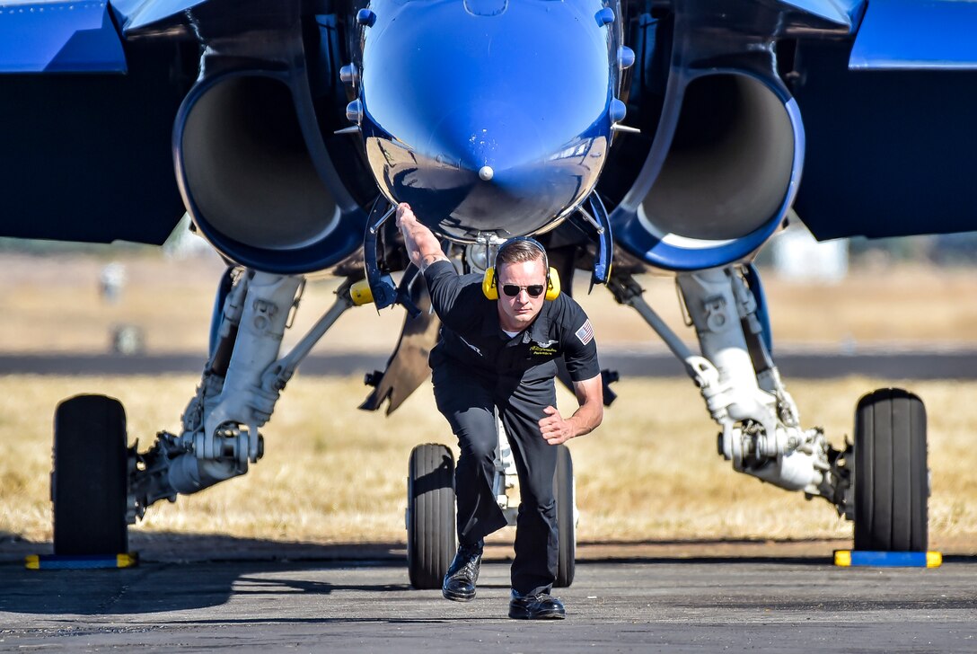 A sailor runs in front of a parked blue jet.