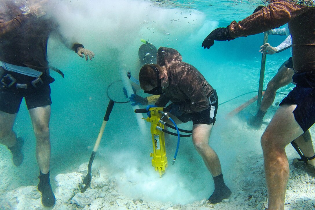 A diver drills underwater as others gather around him.