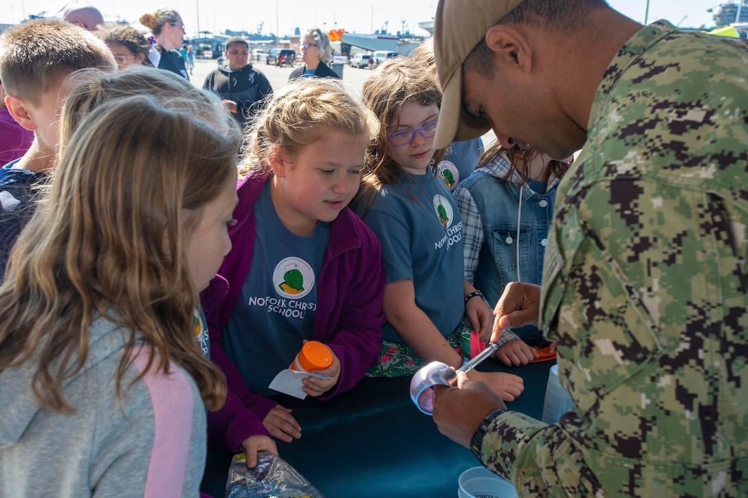 A sailor talks with students crowded at a display table.
