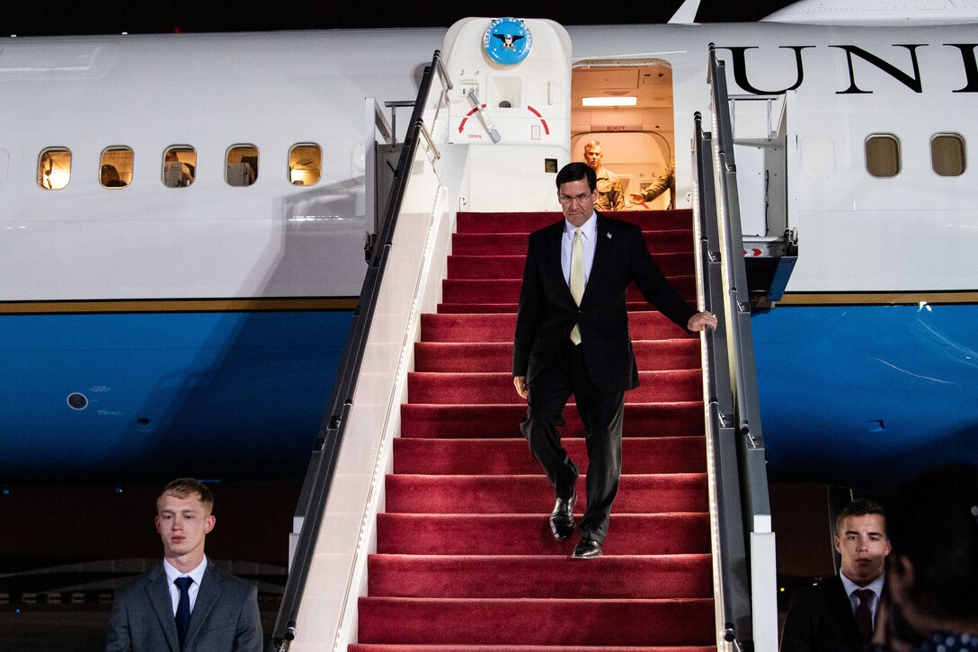 Defense Secretary Dr. Mark T. Esper walks down the steps of a plane.
