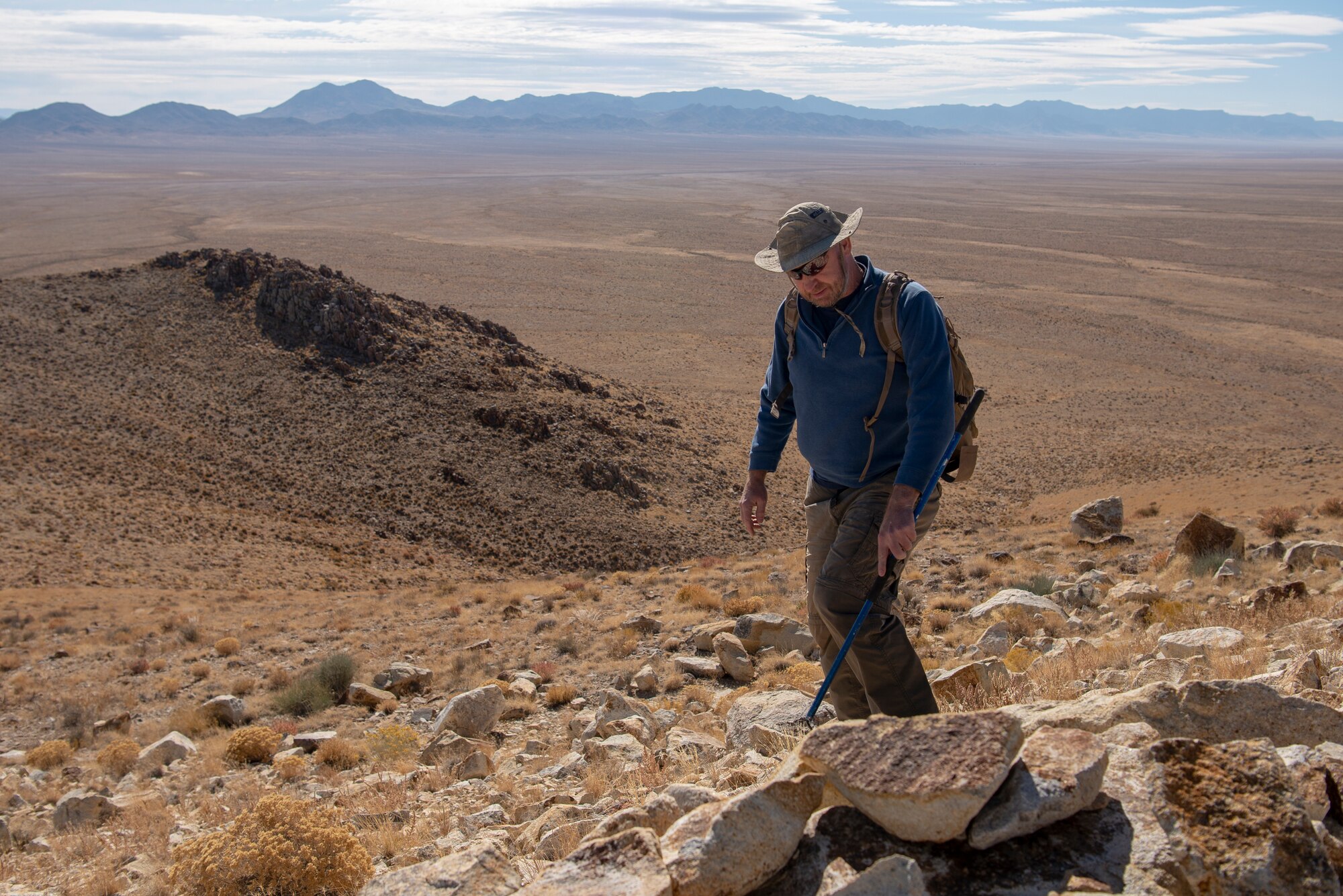 Steve Stocking, lead herpetologist with Colorado State University, scans the hillside for rattlesnakes on the Nellis Test and Training Range, Nevada, Oct. 17, 2019. Stocking partners with the 99th Civil Engineer Squadron to conduct reptile surveys at known rattlesnake den sites. (U.S. Air Force photo by Staff. Sgt. Tabatha McCarthy)