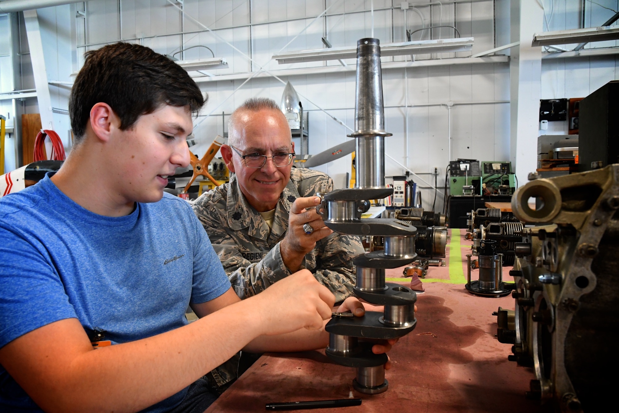 Lt Col. Stan Paregien, 932nd Airlift Wing public affairs officer, speaks with Lincoln Land College Aviation program students and staff Sept. 30, 2019, as part of a community outreach to share news and opportunities to serve in the Air Force Reserve within Illinois.  Charles Oakes shows the colonel how to use a connecting rod on the crankshaft of a Continental A65 Reciprocating engine inside the instructive facility.  (Photo by David Pietrzak, Aviation Program Instructor)