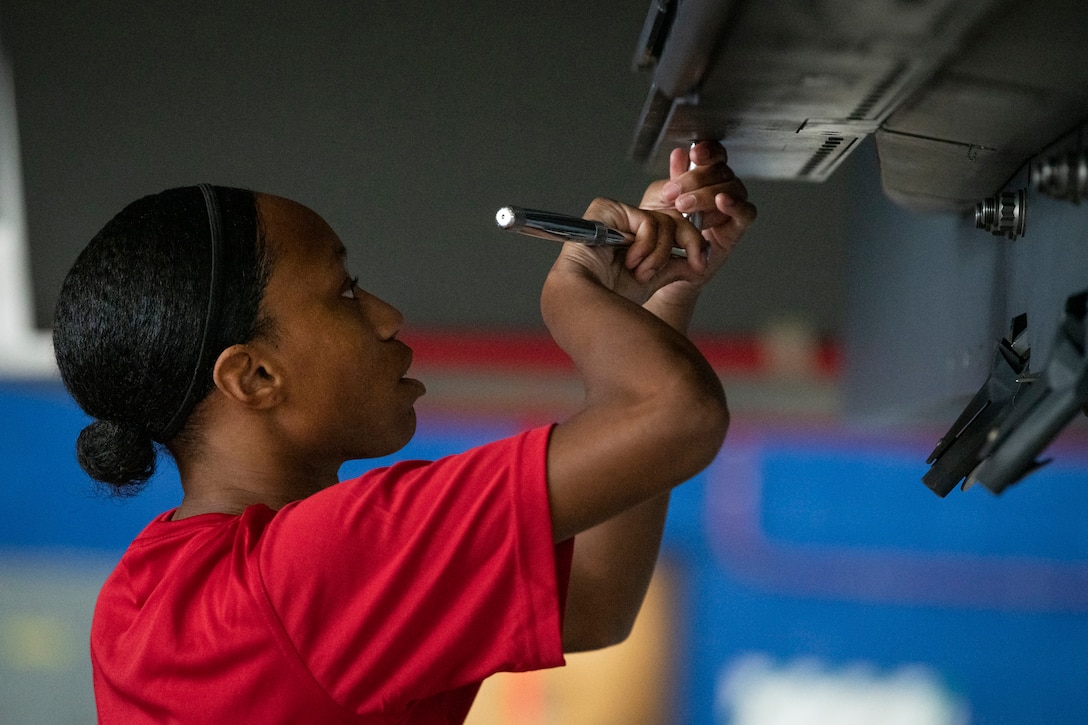 An airman uses a tool on an aircraft.