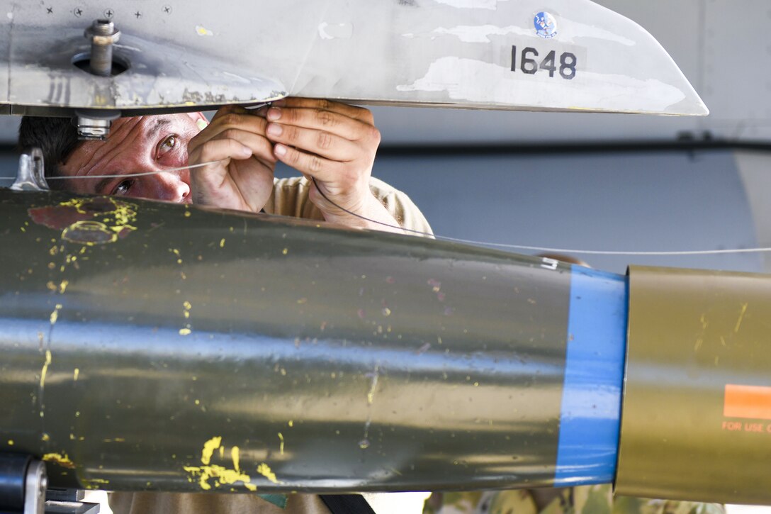 An airman uses tools to attach a bomb to a plane.
